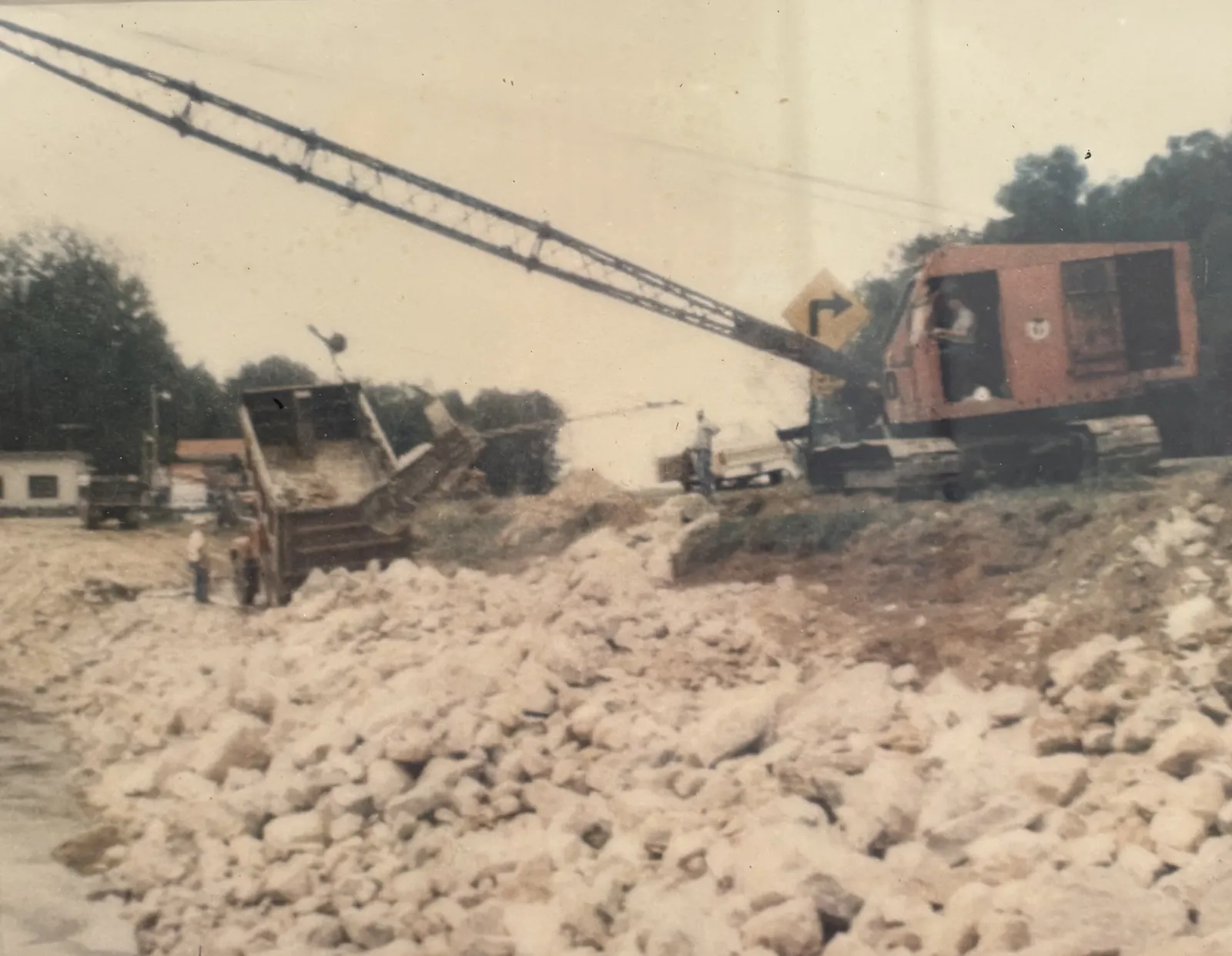 A red crane loading rock along a 1990s channel improvement job