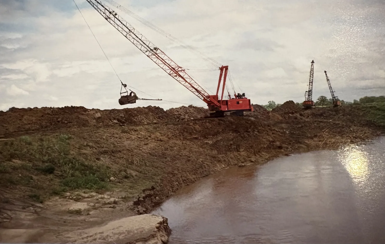 A line of red draglines shaping a levee beside the river on an early RKE flood-control project