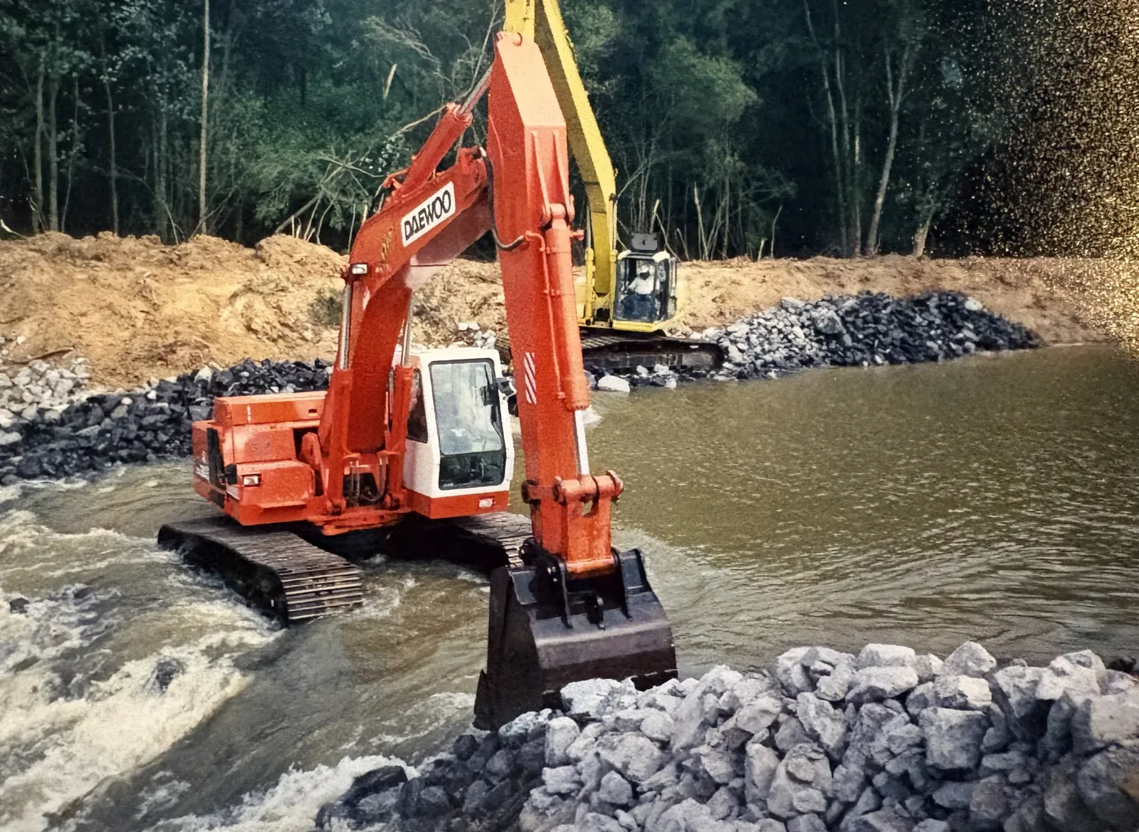 Two excavators placing rock riprap across a flowing creek