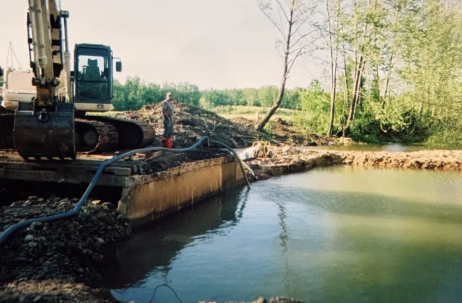 An excavator dewatering a creek diversion during channel work