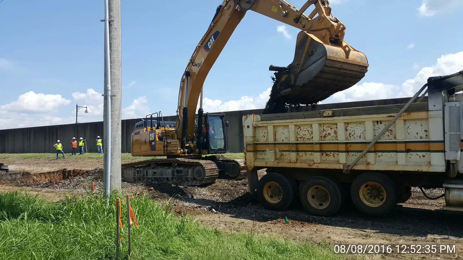 Excavator loading a dump truck during floodwall earthwork